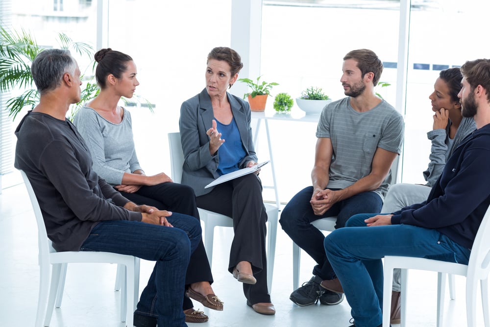 Group therapy in session sitting in a circle in a bright room